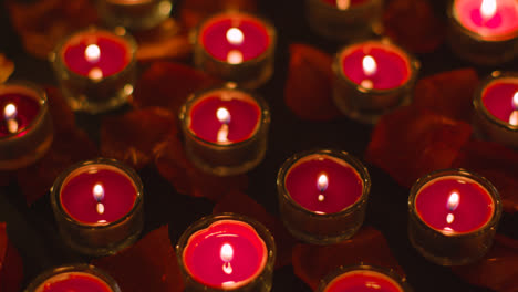 Romantische-Brennende-Rote-Kerzen,-Die-Sich-Auf-Einem-Mit-Rosenblättern-Bedeckten-Hintergrund-Drehen